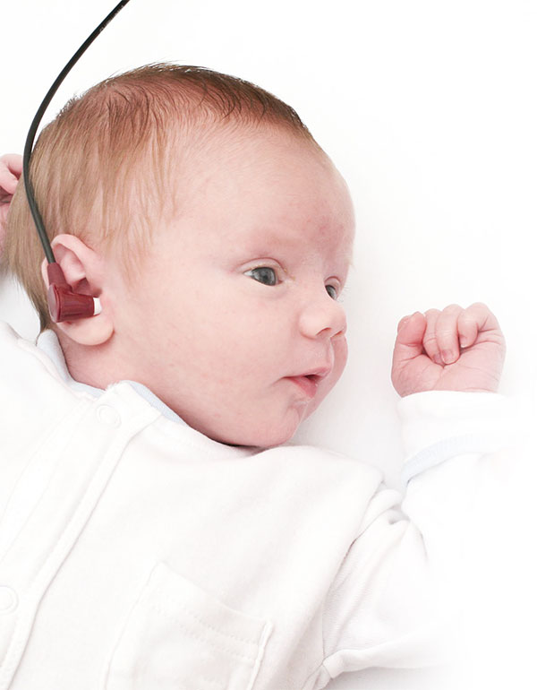 Ein Baby liegt am Rücken und hat die Sonde für das Neugeborenen-Hörscreening im rechten Ohr.